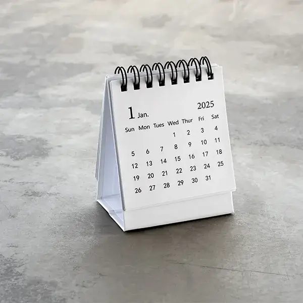 Minimalist white spiral-bound desk calendar open to January 2025 on a gray concrete surface.